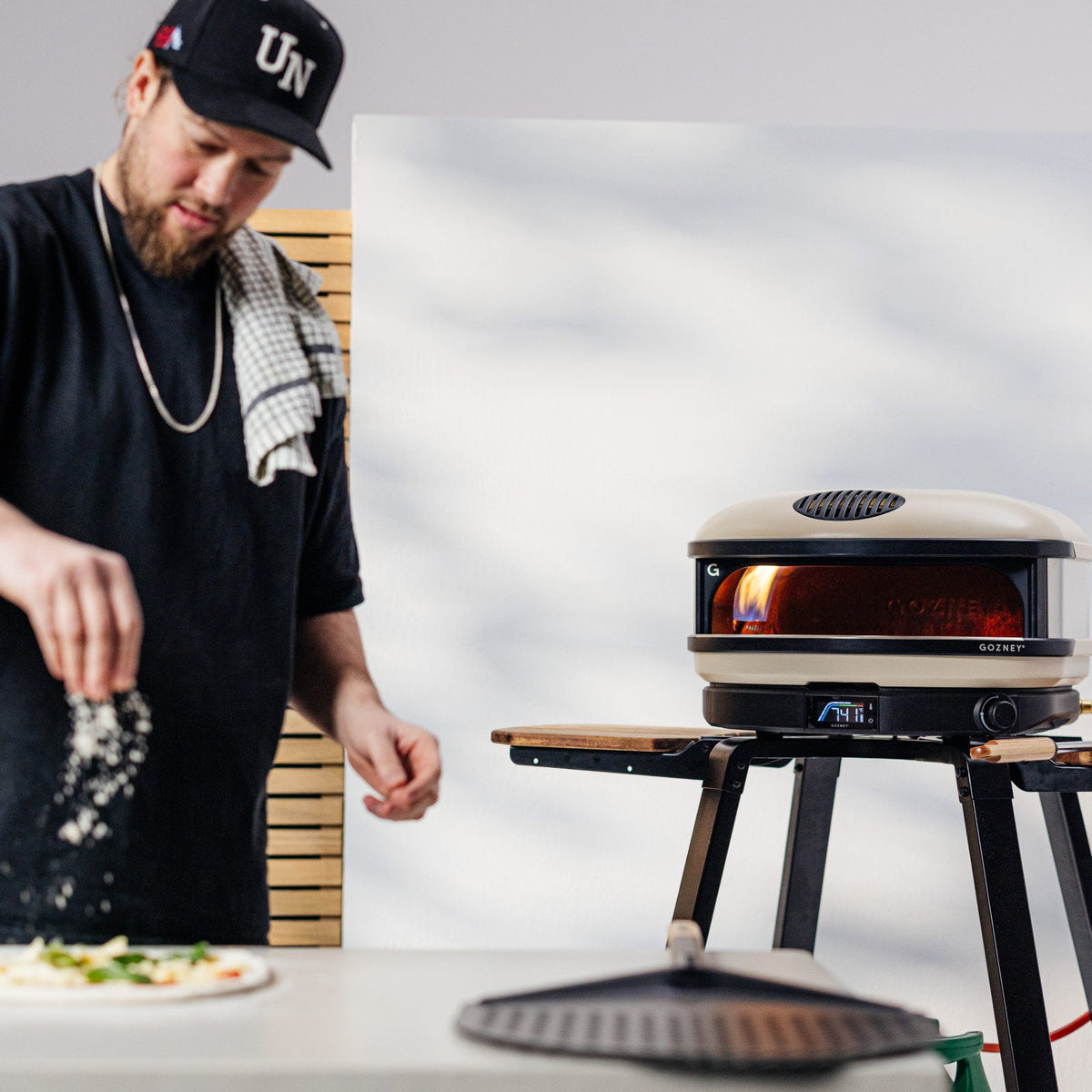 Chef seasoning a pizza beside the Gozney Arc XL in Bone