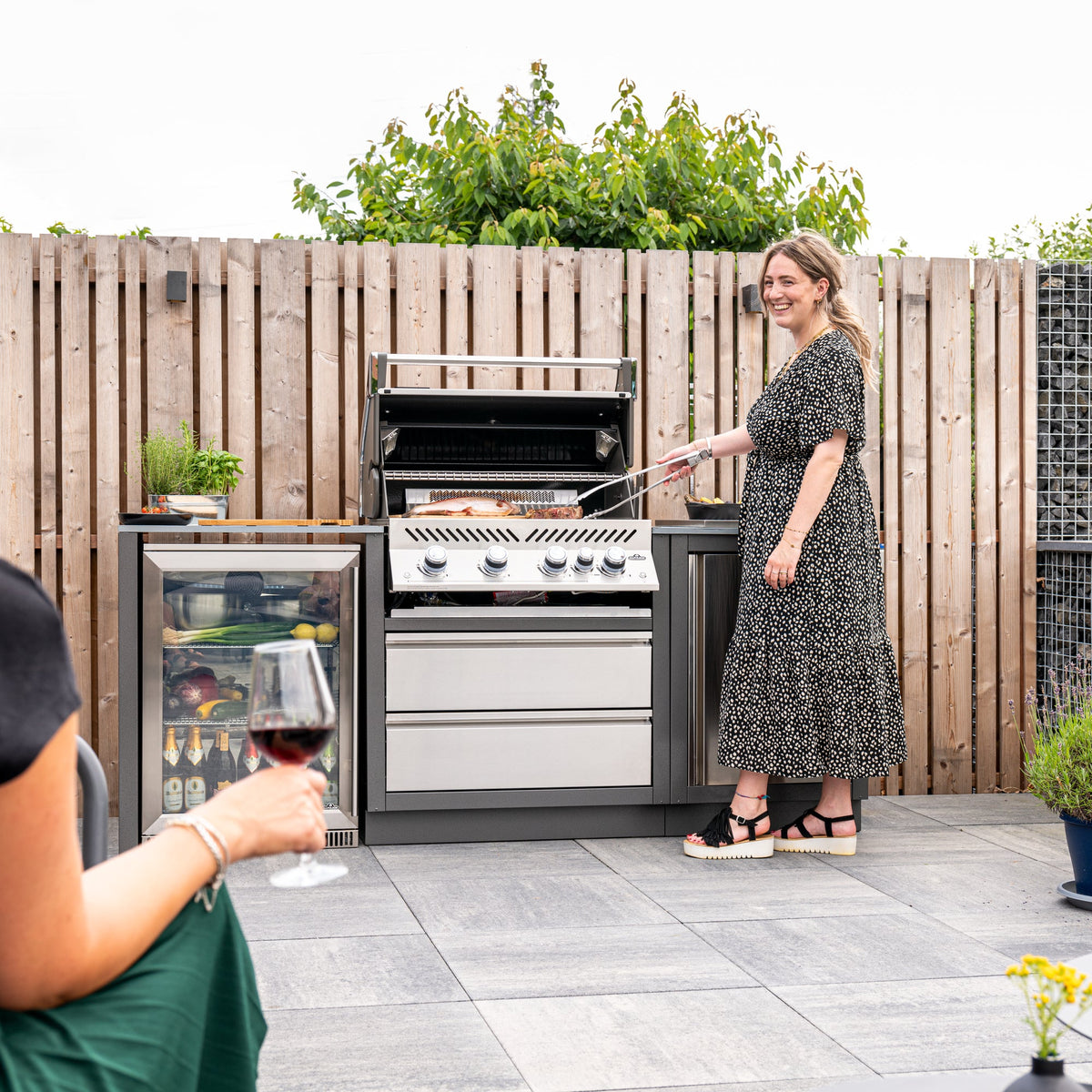 Woman cooking on the Napoleon Prestige PRO 500 Built-In while friends relax with wine