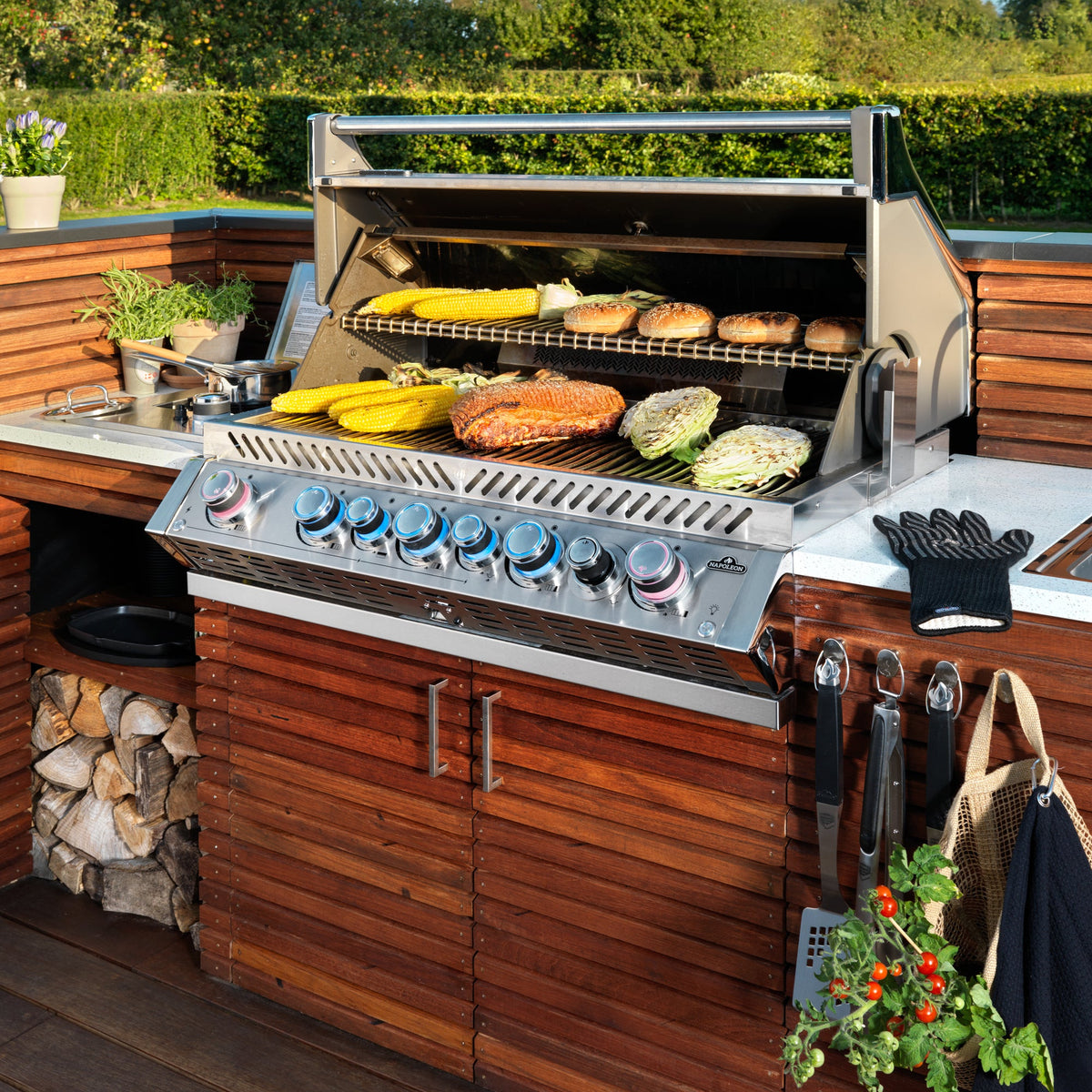 Napoleon Prestige PRO 665 Built-In with the lid open, grilling corn and burgers in an outdoor kitchen