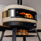 Gozney Dome (Gen 2) in Bone with a wood fire burning and logs stored below