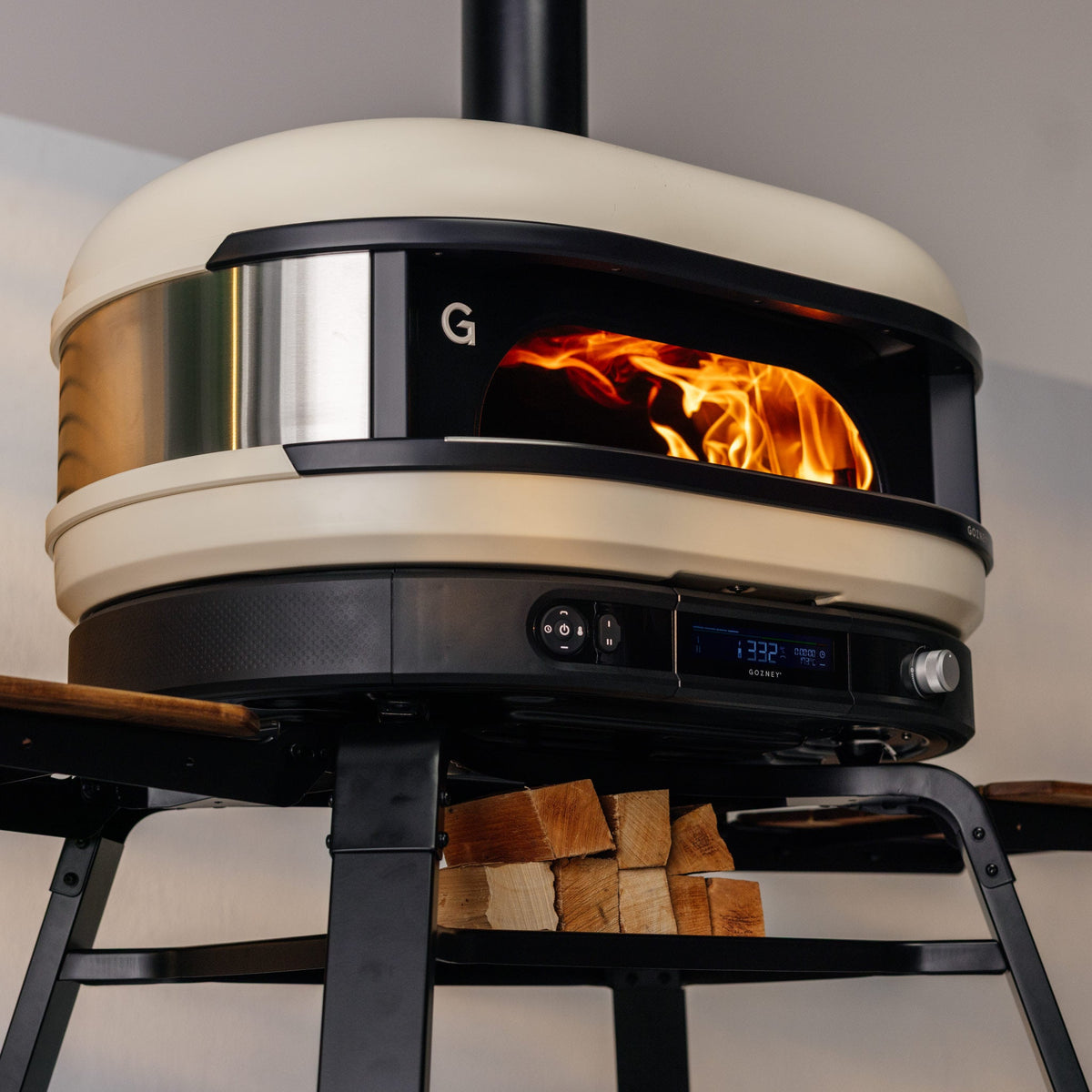 Gozney Dome (Gen 2) in Bone with a wood fire burning and logs stored below
