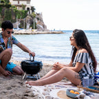 Couple using the Napoleon NK14 Portable Charcoal Kettle on the beach