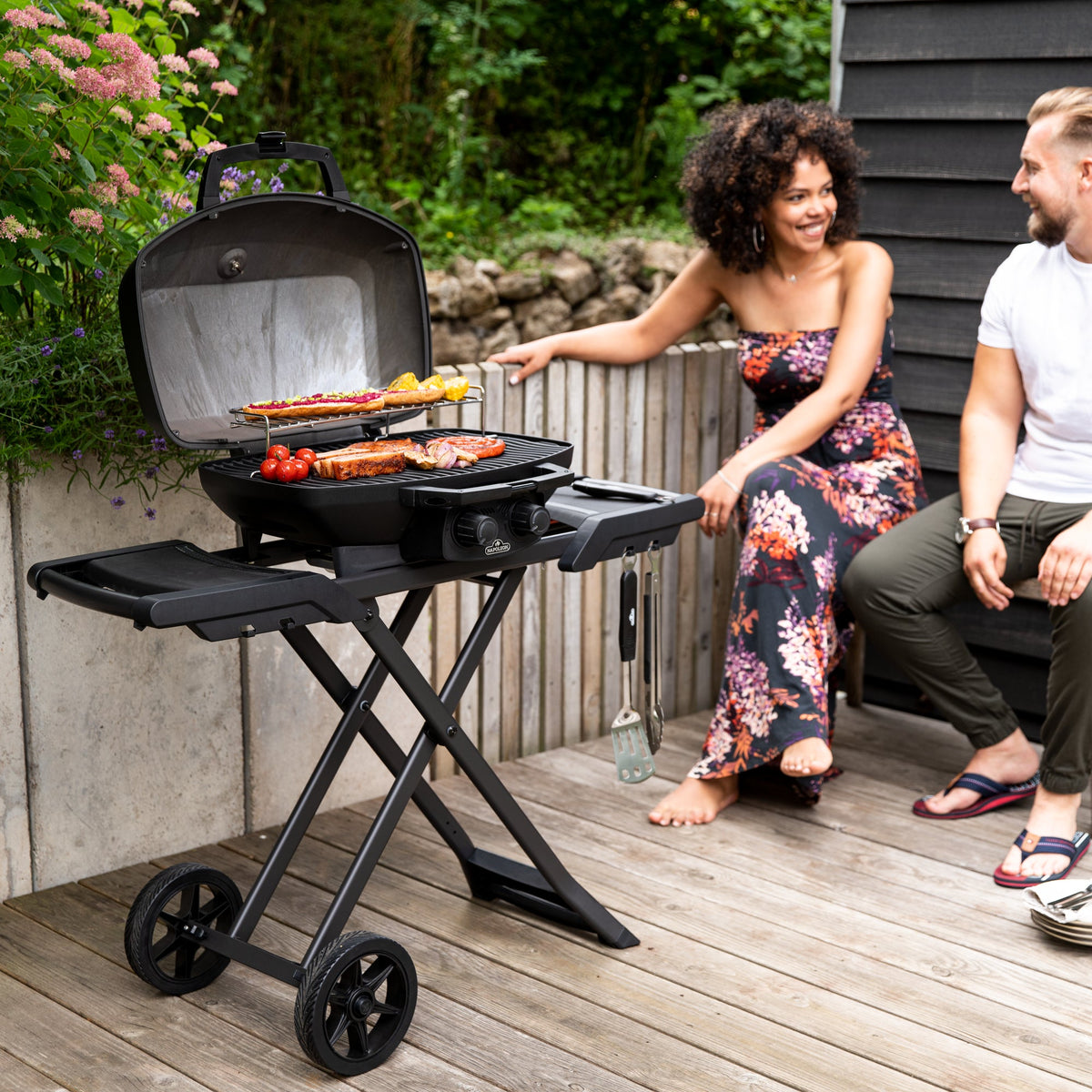 Couple relaxing beside the Napoleon Phantom TravelQ PRO285X while food cooks