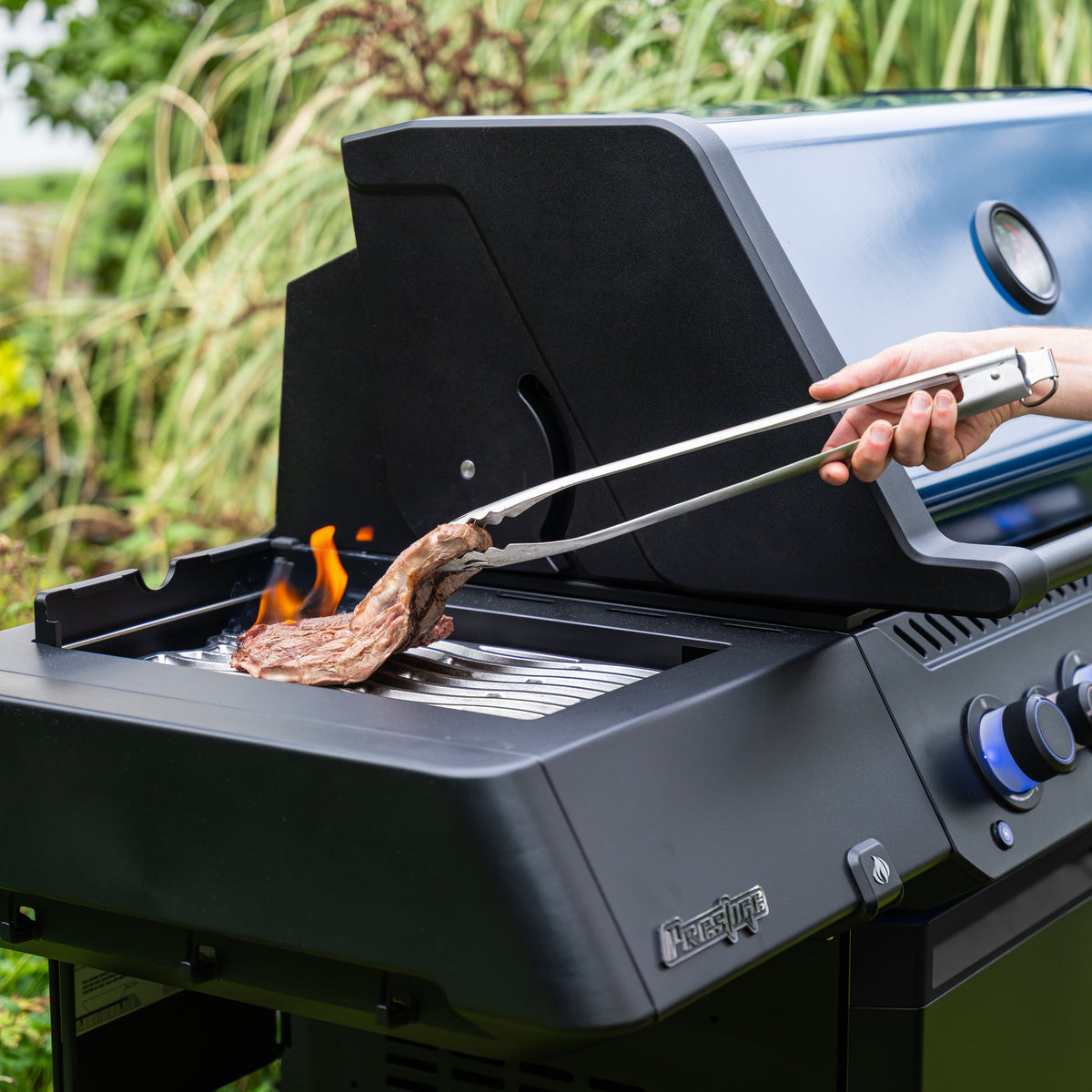 Steak being turned with tongs on the Napoleon Prestige 500 50th Anniversary Edition