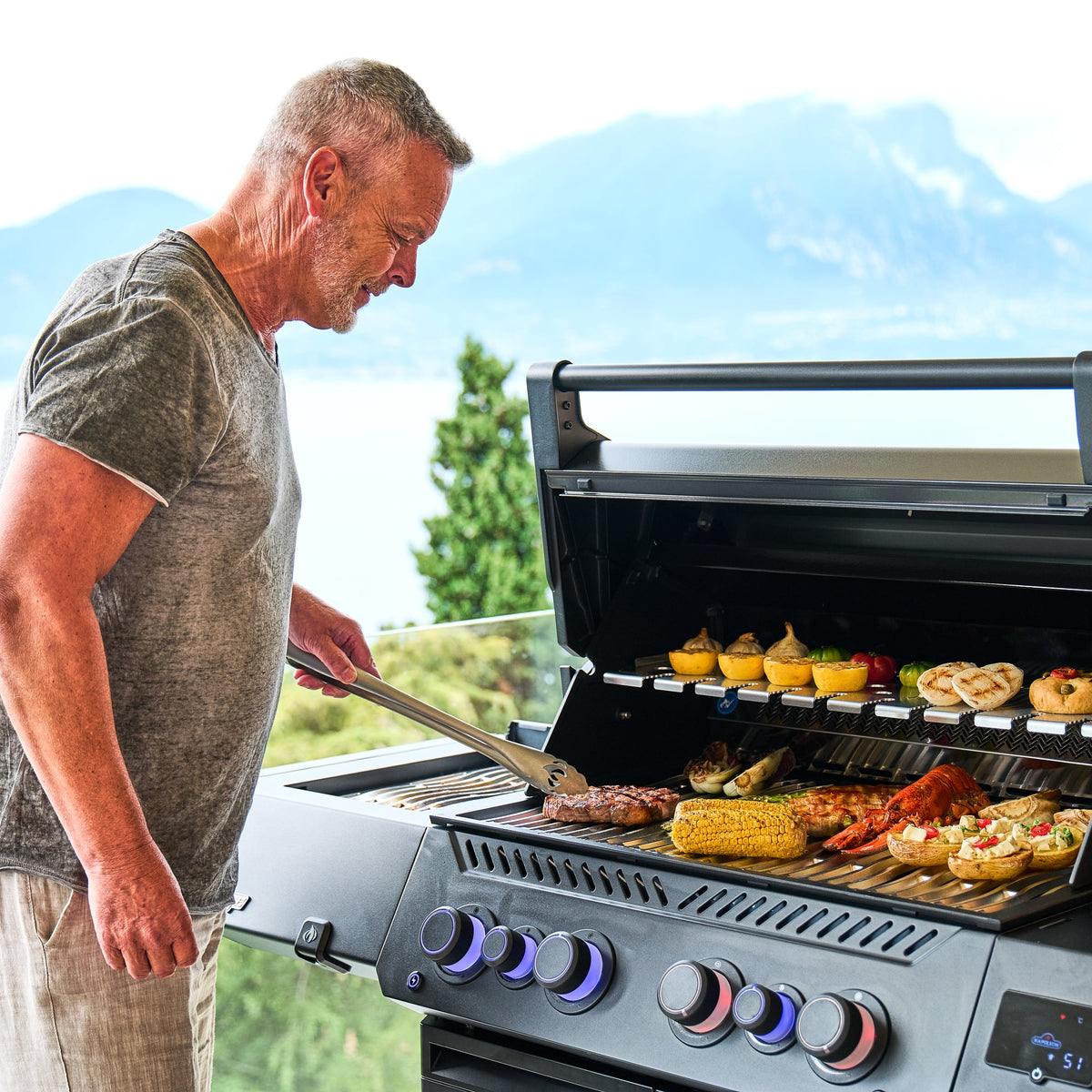 Man grilling corn and skewers on the Napoleon Prestige 500 Phantom Connected with a lake view