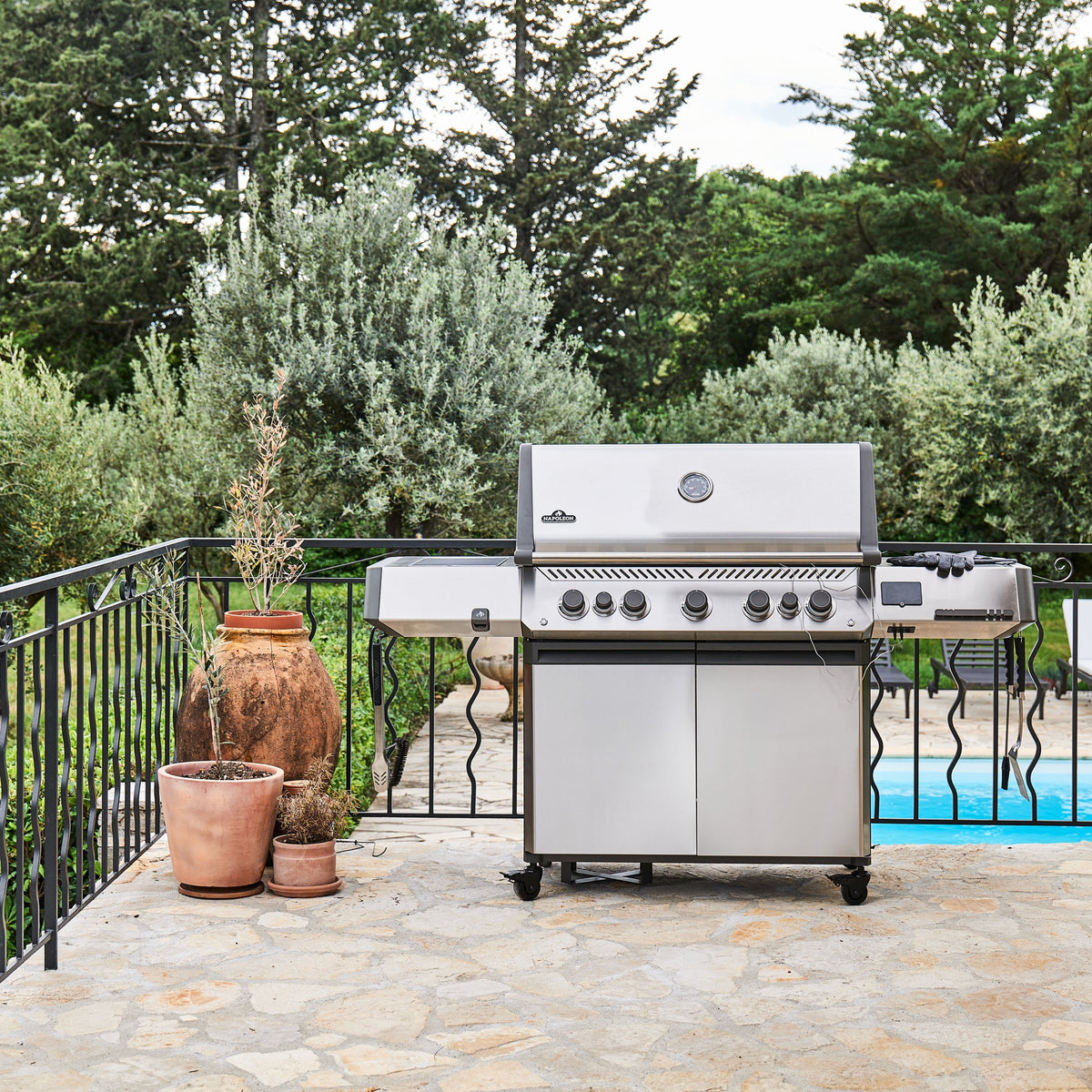 Napoleon Prestige 665 Connected Gas BBQ on a stone terrace beside a swimming pool