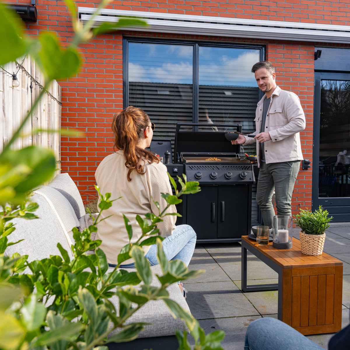 Man cooking on the Napoleon Rogue PRO Phantom 30 Plancha while a friend relaxes nearby