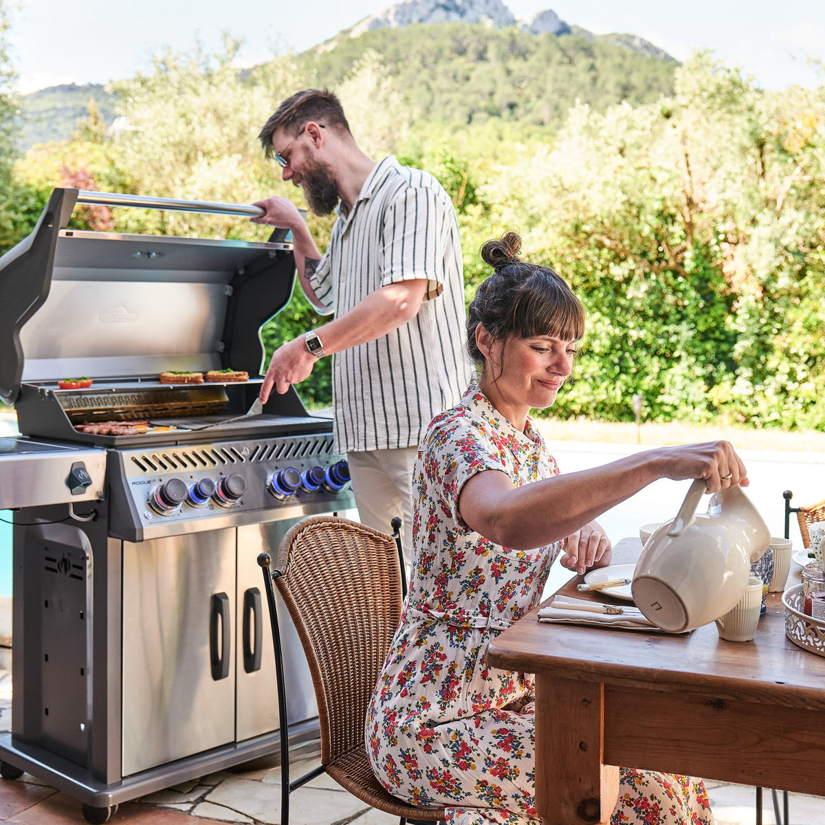 Man cooking on the Napoleon Rogue PRO-S 525 while breakfast is served on the terrace